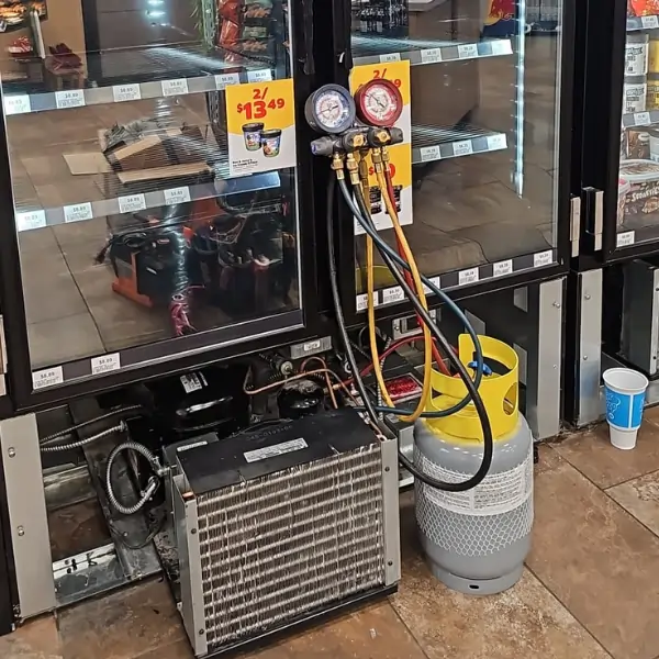 Commercial refrigeration technician servicing a store cooler using pressure gauges and refrigerant tank during repair in Calgary – Express Refrigeration Ltd HVAC and refrigeration specialists